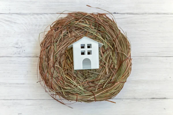 Miniature white toy model house rests in nest on rustic old vintage white wooden background. Eco village environmental real estate mortgage property insurance dream home ecology investment concept