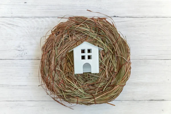 Minyatür beyaz oyuncak model ev yuvada rustik eski vintage beyaz ahşap arka plan üzerinde duruyor. Eko köyü çevre gayrimenkul ipotek Emlak sigorta rüya ev ekoloji yatırım kavramı