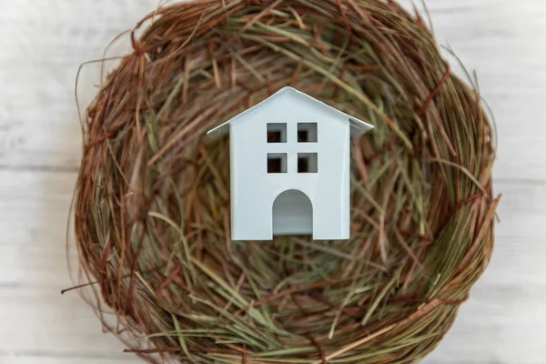 Minyatür beyaz oyuncak model ev yuvada rustik eski vintage beyaz ahşap arka plan üzerinde duruyor. Eko köyü çevre gayrimenkul ipotek Emlak sigorta rüya ev ekoloji yatırım kavramı