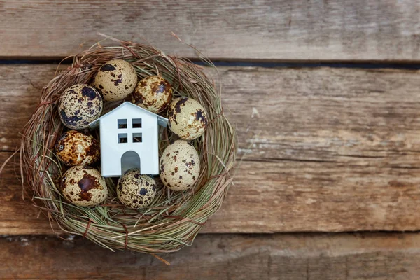 Miniature white toy model house rests in nest with eggs on rustic old vintage wooden background. Eco village environmental real estate mortgage property insurance dream home ecology investment concept