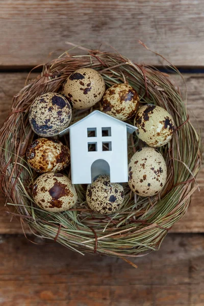 Miniature white toy model house rests in nest with eggs on rustic old vintage wooden background. Eco village environmental real estate mortgage property insurance dream home ecology investment concept