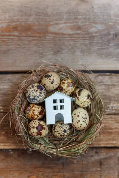 Miniature white toy model house rests in nest with eggs on rustic old vintage wooden background. Eco village environmental real estate mortgage property insurance dream home ecology investment concept