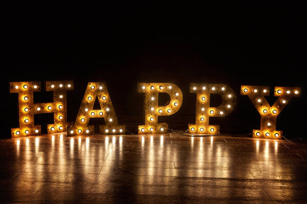 Счастливые буквы слово с светящимися лампочками ретро стоя на полу
