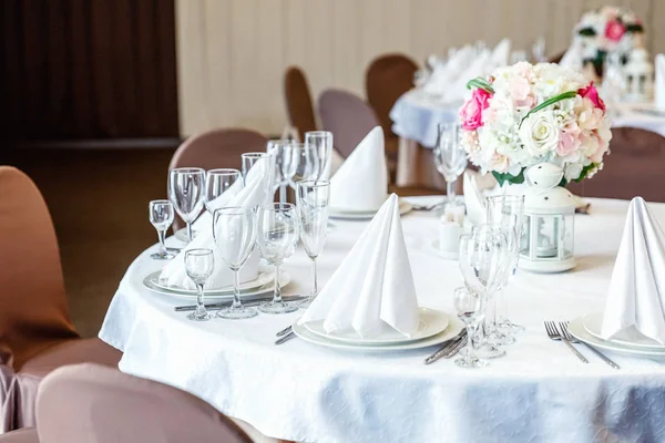 Gözlük, çiçekler, çatal, bıçak, bir piramit katlanmış peçete rahat iç restoranda akşam yemeği için hizmet. Düğün süslemeleri ve maddeler için gıda, beyaz masa örtüsü ile kaplı büyük bir tabloda catering hizmeti göre düzenlenmiş