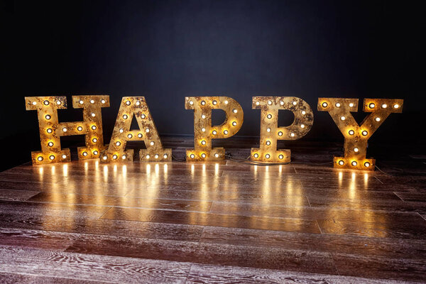 Счастливые буквы слово с светящимися лампочками ретро стоя на полу
