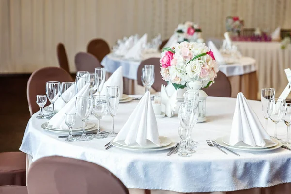 Gözlük, çiçekler, çatal, bıçak, bir piramit katlanmış peçete rahat iç restoranda akşam yemeği için hizmet. Düğün süslemeleri ve maddeler için gıda, beyaz masa örtüsü ile kaplı büyük bir tabloda catering hizmeti göre düzenlenmiş
