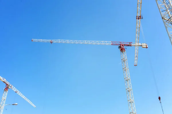 Cranes and workers at construction site against blue sky