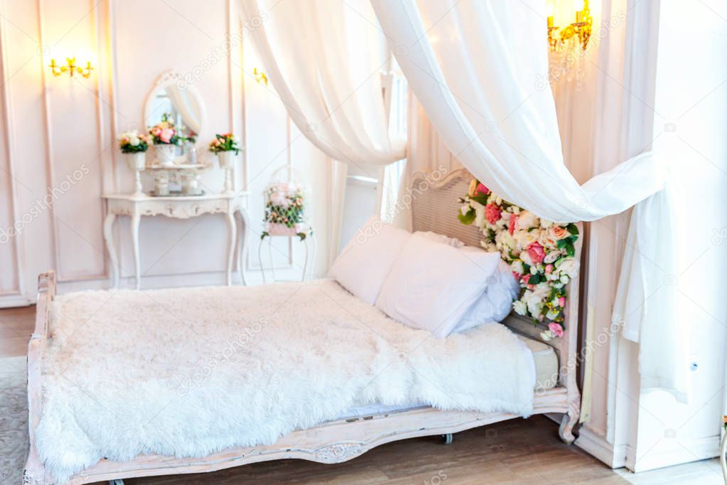 Beautiful luxury classic white bright clean interior bedroom in baroque style with king-size bed, large window, armchair and flower composition