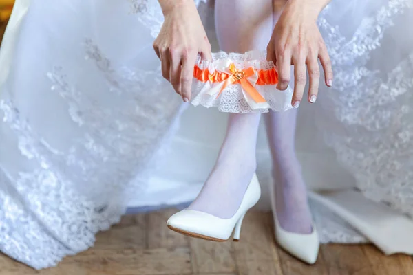 Garter on the leg of a bride, slim sexy bride in wedding luxury dress showing her silk garter. woman have a final preparation for wedding ceremony. Wedding day moments