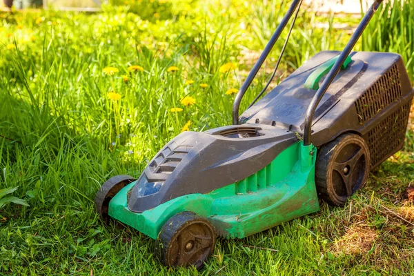 Lawn mower cutting green grass in backyard in sunny day. Gardening country lifestyle background. Beautiful view on fresh green grass lawn in sunlight, garden landscape in spring or summer season
