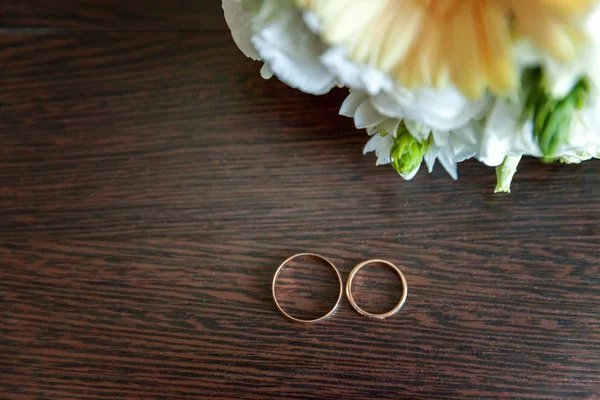Krásné Snubní Prsteny Leží Stole Pozadí Kytici Květin — Stock fotografie