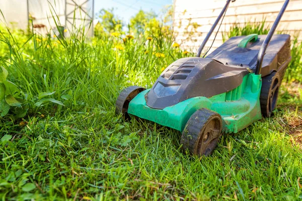 Lawn mower cutting green grass in backyard in sunny day. Gardening country lifestyle background. Beautiful view on fresh green grass lawn in sunlight, garden landscape in spring or summer season