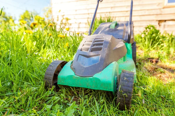 Lawn mower cutting green grass in backyard in sunny day. Gardening country lifestyle background. Beautiful view on fresh green grass lawn in sunlight, garden landscape in spring or summer season