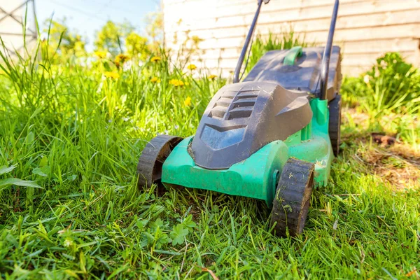 Lawn mower cutting green grass in backyard in sunny day. Gardening country lifestyle background. Beautiful view on fresh green grass lawn in sunlight, garden landscape in spring or summer season