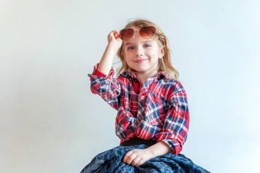 Küçük kız hipster hippi Çingene kovboy beyaz poz modern sandalye üzerinde oturan güneş gözlüğü gibi giyinmiş genç tatlı mutlu çok güzel moda hafif parlak Oda arka planda duvar. Yaşam tarzı insanların moda kavramı