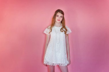Mutlu genç kız gülümsüyor. Beyaz elbise ayakta pembe renkli pastel trendy modern moda pin-up arka plan üzerinde giyen portre portre genç mutlu pozitif kadın. Avrupa kadın. Olumlu insan duygu yüz ifadesi beden dili