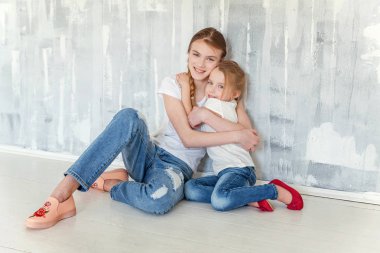 Gri desenli duvar arka planı oturma ve kucaklayan iki mutlu çocuk. Sevimli sevimli küçük kız onun sevgi ve bakım gösterilen sıkı Şirin genç kız, sarılma. Kız evde eğlenmek