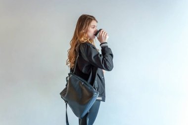 Kağıt bardak tutan ve kahve içme genç Genç kız beyaz duvara, deri ceketli. Sıradan günlük yaşam. Hipster rock tarzı kıyafet giymiş seksi moda şehvetli kadın