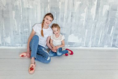 Gri desenli duvar arka planı oturma ve kucaklayan iki mutlu çocuk. Sevimli sevimli küçük kız onun sevgi ve bakım gösterilen sıkı Şirin genç kız, sarılma. Kız evde eğlenmek