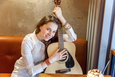 Gitar çalmak kafede oturan genç gülümseyen hipster kadın. Şarkı çalmayı kız