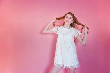 Mutlu genç kız gülümsüyor. Beyaz elbise ayakta pembe renkli pastel trendy modern moda pin-up arka plan üzerinde giyen portre portre genç mutlu pozitif kadın. Avrupa kadın. Olumlu insan duygu yüz ifadesi beden dili