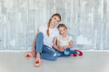 Gri desenli duvar arka planı oturma ve kucaklayan iki mutlu çocuk. Sevimli sevimli küçük kız onun sevgi ve bakım gösterilen sıkı Şirin genç kız, sarılma. Kız evde eğlenmek