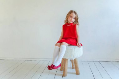 Mutlu küçük kız beyaz duvar arka planda parlak oda karşı sandalyeye oturan kırmızı elbiseli