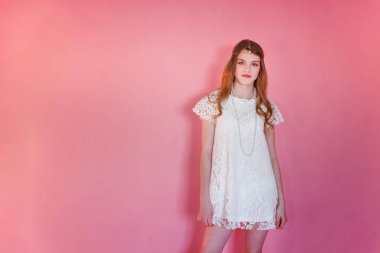 Mutlu genç kız gülümsüyor. Beyaz elbise ayakta pembe renkli pastel trendy modern moda pin-up arka plan üzerinde giyen portre portre genç mutlu pozitif kadın. Avrupa kadın. Olumlu insan duygu yüz ifadesi beden dili