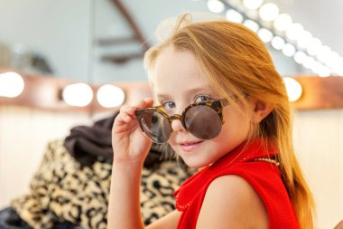 Bir kız, bir çocuk, bir model güzel elbise ve ayna lambalar ile oturma ve gülümseyen güneş gözlüğü. Tarzı çocuk güzellik salonu photosession kavramı