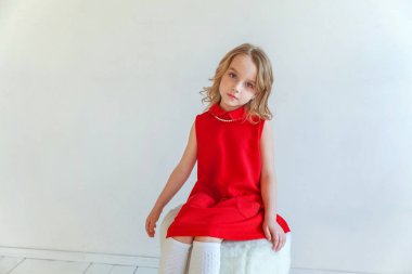 Mutlu küçük kız beyaz duvar arka planda parlak oda karşı sandalyeye oturan kırmızı elbiseli