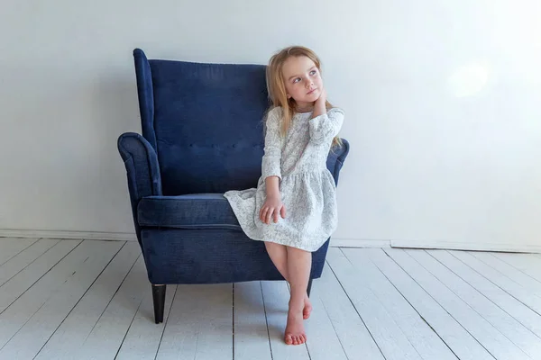 白のリビング ルームでリラックスしたモダンな居心地の良い青い椅子に座っている灰色の服を自宅でかわいい女の子 — ストック写真