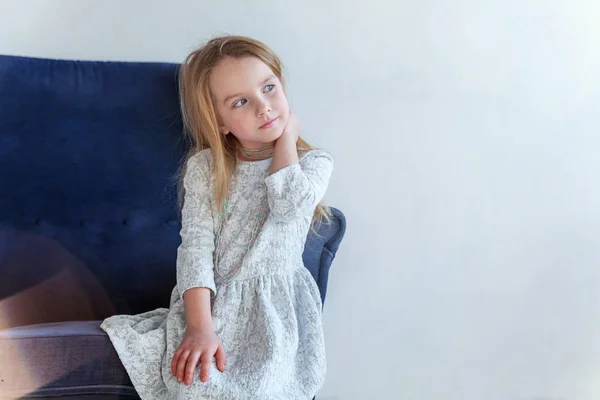 白のリビング ルームでリラックスしたモダンな居心地の良い青い椅子に座っている灰色の服を自宅でかわいい女の子 — ストック写真
