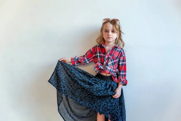 Sweet happy adorable fashion young little girl dressed like hipster hippie gipsy cowboy in sunglasses standing against white wall background in light bright room. Lifestyle people trendy concept