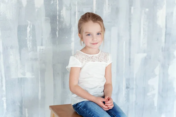グレー テクスチャ壁の背景に椅子に座って空の白 シャツで甘い幸せな少女 — ストック写真