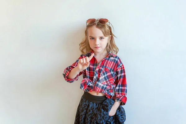 Sweet happy adorable fashion young little girl dressed like hipster hippie gipsy cowboy in sunglasses standing against white wall background in light bright room. Lifestyle people trendy concept