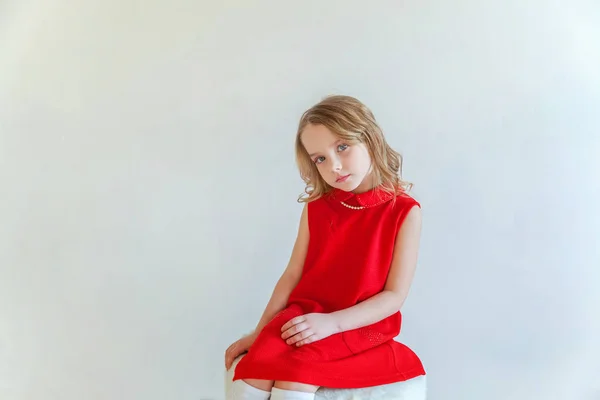 明るい部屋で白い壁背景に椅子に座っている赤いドレスの甘い幸せな少女 — ストック写真