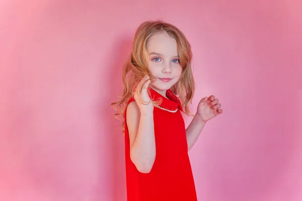 Little cute sweet smiling girl in red dress standing on pink colourful pastel trendy modern fashion pin-up background