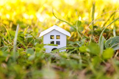 Miniature white toy model house in meadow with grass. Eco Village, abstract environmental background. Real estate mortgage property insurance dream home ecology concept clipart