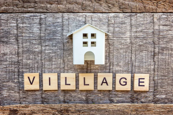 Miniature toy model house with inscription VILLAGE letters word on wooden backdrop. Eco Village, abstract environmental background. Real estate mortgage property insurance sweet home ecology sale concept