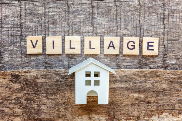 Miniature toy model house with inscription VILLAGE letters word on wooden backdrop. Eco Village, abstract environmental background. Real estate mortgage property insurance sweet home ecology sale concept