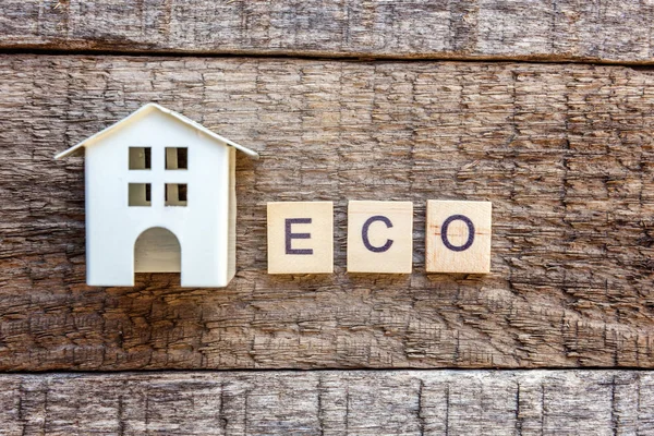 Miniature toy model house with inscription ECO letters word on wooden backdrop. Eco Village, abstract environmental background. Real estate mortgage property insurance sweet home ecology concept