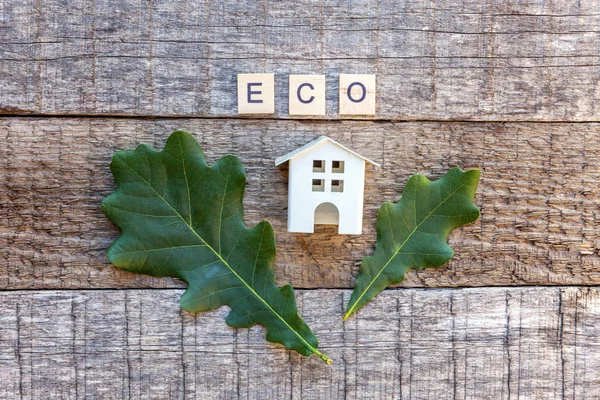 Miniature toy model house with inscription ECO letters word on wooden backdrop. Eco Village, abstract environmental background. Real estate mortgage property insurance sweet home ecology concept