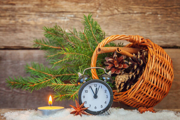 Christmas New Year composition winter objects fir branch basket pine cones candle alarm clock on old rustic wooden background. Xmas holiday december decoration copy space. Time for celebration concept