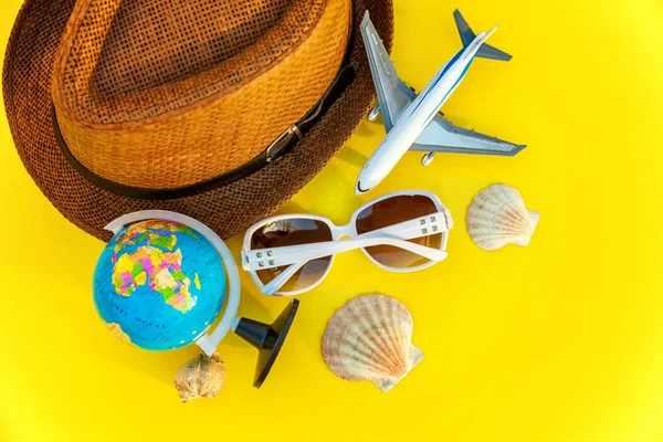 Flat Lay with hat, globe, plane, sunglasses and shell on yellow colourful trendy modern fashion background. Vacation travel summer weekend sea adventure trip concept