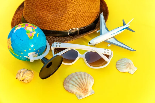 Flat Lay with hat, globe, plane, sunglasses and shell on yellow colourful trendy modern fashion background. Vacation travel summer weekend sea adventure trip concept