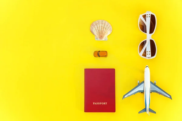 Flat Lay with plane, passport, sunglasses and shell on yellow colourful trendy modern fashion background. Vacation travel summer weekend sea adventure trip concept