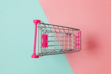 Küçük süpermarket bakkal itme sepeti tekerlekli alışveriş oyuncak için mavi ve pembe pastel renkli kağıt trendy geometrik arka plan üzerinde kopya alanı izole. Satılık satın Alışveriş Merkezi Pazar dükkanı tüketici kavramı