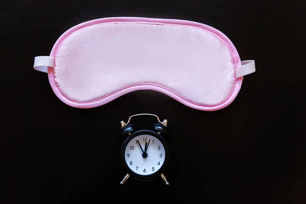 Sleeping eye mask, alarm clock isolated on dark black background. Do not disturb me, let me sleep. Rest, good night, siesta, insomnia, relaxation, tired, travel concept