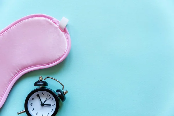 Sleeping eye mask, alarm clock isolated on blue pastel colourful trendy background. Do not disturb me, let me sleep. Rest, good night, siesta, insomnia, relaxation, tired, travel concept