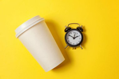 Sadece düz yatıyordu tasarım kağıt kahve Kupası ve sarı renkli şık arka planda çalar saat. Paket servisi olan restoran içki ve kahvaltı içecek. Günaydın uyanık kavramı uyandır. Üstten görünüm kopya alanı